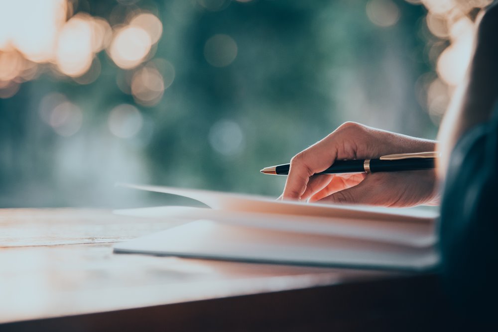 Person writing in notebook with pen